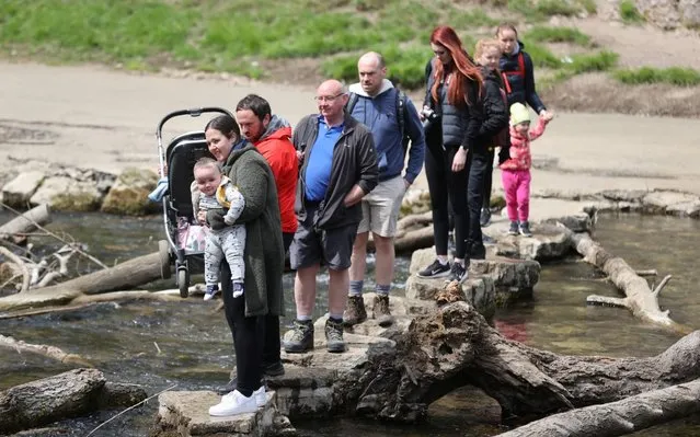 People walk on rocks to cross the River Dove in Dovedale in the Peak District, following the outbreak of the coronavirus disease (COVID-19), Ashbourne, Britain, May 16, 2020. (Photo by Carl Recine/Reuters)