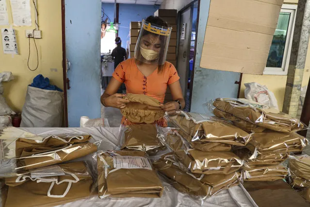 A woman wearing face mask and face shield to help curb the spread of the new coronavirus, checks surgical gown at a packing session at a garment factory Thursday, May 28, 2020, at Industrial Zone in Yangon, Myanmar. Despite a poor public health infrastructure and crowded urban areas, Myanmar has reported a surprising low number of COVID-19 cases, with just a little over 200 confirmed and a few deaths. (Photo by Thein Zaw/AP Photo)