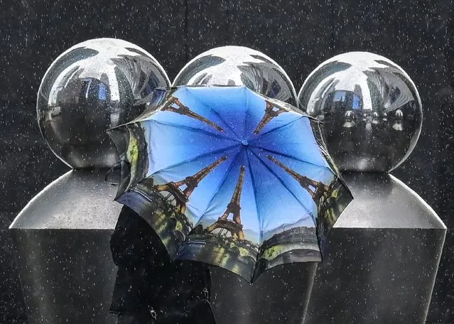A pedestrian walks past modern art sculptures under an umbrella during a heavy rain in central Moscow on September 2, 2022. (Photo by Yuri Kadobnov/AFP Photo)