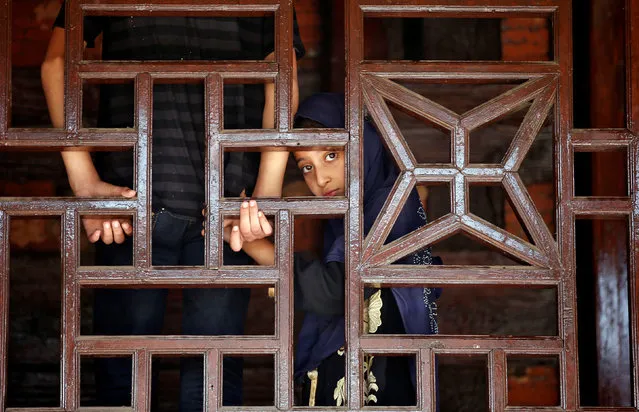 A Muslim girl looks on behind a wooden window frame at the shrine of Mir Syed Ali Hamdani, a Sufi saint, during an annual religious festival in Srinagar, August 29, 2017. (Photo by Danish Ismail/Reuters)