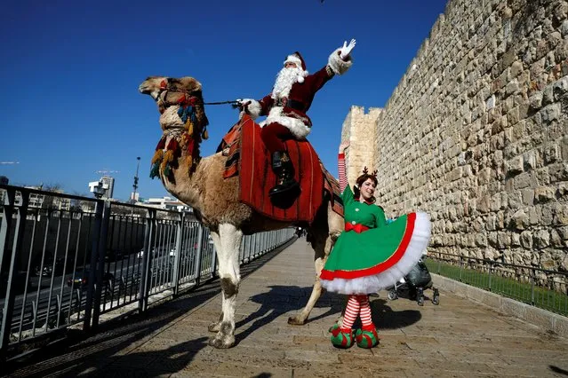 Dressed as Santa Claus, Issa Kassissieh sits astride a camel while a dancer dances next to him, as he visits Jaffa Gate in Jerusalem's Old City on December 22, 2022. (Photo by Ammar Awad/Reuters)