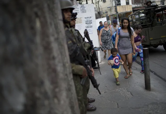 In this September 28, 2017 photo, residents walk past soldiers patrolling the Rocinha slum in Rio de Janeiro, Brazil. Amid a national economic crisis that has exacerbated deep inequality and resulted in funding cuts for security forces, authorities admit they have again lost control of most slums they once said had been “pacified”. (Photo by Silvia Izquierdo/AP Photo)