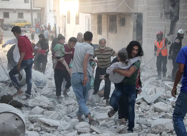 Syrian men carry injured people amid the rubble of destroyed buildings following a reported air strike on the rebel-held northwestern city of Idlib on September 29, 2016. In a statement the Syrian Observatory for Human Rights said that at least five air strikes hit various areas in the city of Idlib. (Photo by Omar Haj Kadour/AFP Photo)