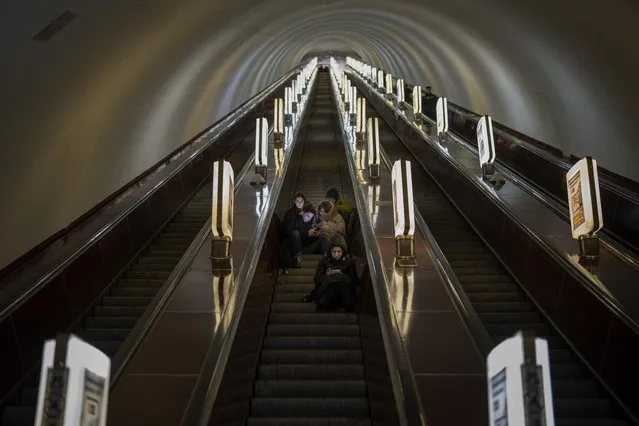 People sit on an inactive escalator in a subway station being used as a bomb shelter during an air siren in Kyiv, Ukraine, Monday, February 20, 2023. President Joe Biden made an unannounced visit to Ukraine on Monday to meet with President Volodymyr Zelenskyy, a striking gesture of solidarity that comes days before the one-year anniversary of Russia's invasion of the country. (Photo by Emilio Morenatti/AP Photo)