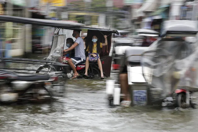 Residents wearing masks to prevent the spread of the coronavirus ride motorcycles as they negotiate a flooded road due to Typhoon Molave in Pampanga province, northern Philippines on Monday, October 26, 2020. (Photo by Aaron Favila/AP Photo)