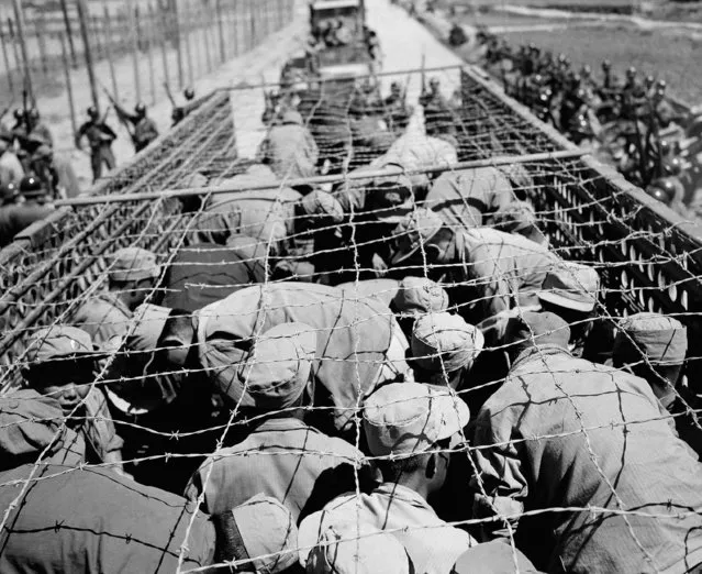 North Korean prisoners huddle under barbed wire as they are transported from one compound to another on Koje Island, June 17, 1952. They are surrounded by guards on either side of the road. Allied command moved 22,500 Communist Prisoners of War out of four large compounds without any opposition. The meekness of the prisoners left no doubt that Brig. Gen. Haydon L. Boatner had gained unchallenged control over 80,000 prisoners who only one week earlier ran their compounds unhindered and defied their captors. (Photo by AP Photo)