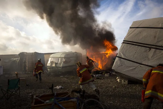 Workers trying to extinguish a tent burning at a makeshift migrant camp known as “the jungle” near Calais, northern France, Thursday, October 27, 2016. French authorities claimed on Wednesday that they had cleared the makeshift migrant camp near the northern French city of Calais. (Photo by Emilio Morenatti/AP Photo)