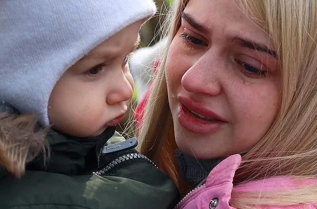 A woman is in tears as she holds her child after fleeing from Ukraine because of the Russian invasion as they arrived with a bus at the village of Moszczany near the border checkpoint at Korczowa, Poland, March 1, 2022. (Photo by Kai Pfaffenbach/Reuters)