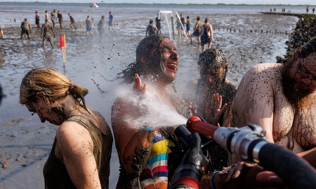 Participants covered in mud are seen as they are showered off after taking part in a world record in making mud angels as part of the 2024 Mud Flats Olympics (20. Wattolümpiade) on August 17, 2024 near Brunsbuetel, Germany. This the twentieth year the Mud Flats Olympics are taking place. Organizers, who say they are getting old, claim it is the last. The event raises money for local charities. (Photo by Morris MacMatzen/Getty Images)
