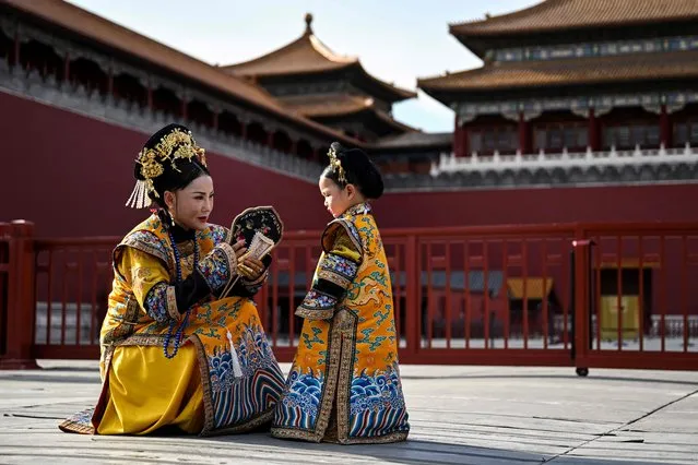 A woman and a girl wearing a traditional Chinese costume chat next to the Forbidden City during a photo session with a local photographer in Beijing on June 7, 2023. (Photo by Hector Retamal/AFP Photo)