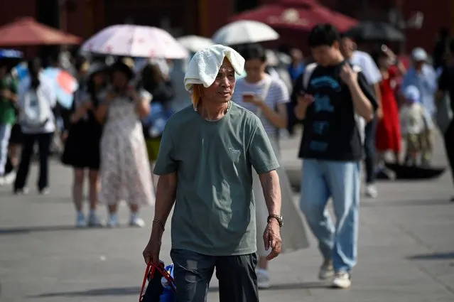 A man shelters under a towel during hot weather conditions in Beijing on June 16, 2023. (Photo by Wang Zhao/AFP Photo)