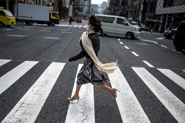 A woman runs to cross a street in Tokyo on March 5, 2021. (Photo by Charly Triballeau/AFP Photo)