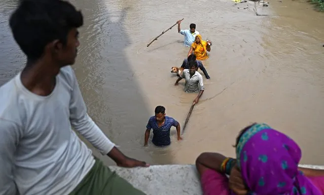 People wade through a flooded street after river Yamuna overflowed following heavy monsoon rains in New Delhi on July 13, 2023. Days of relentless monsoon rains have killed at least 66 people in India, government officials said on July 12, with dozens of foreign tourists stranded in the Himalayas after floods severed road connections. (Photo by AArun Sankar/AFP Photo)