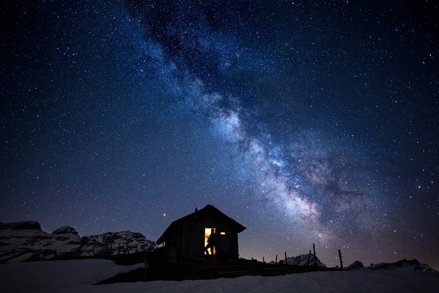 A man looks a starry sky with the milky way early morning from a little cabin at the Ormont Valley, Switzerland, Friday, May 18, 2018. (Photo by Anthony Anex/Keystone via AP Photo)