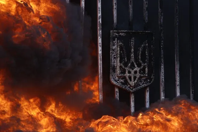 Flames from burning tyres engulf the entrance gates, which bear the Ukrainian national coat of arms, to Ukraine's Defence Ministry during a protest against the disbanding of the “Aydar” battalion in Kiev February 2, 2015. (Photo by Valentyn Ogirenko/Reuters)
