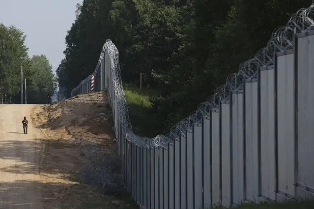 A Polish border guard patrols the area of a newly built metal wall on the border between Poland and Belarus, near Kuznice, Poland, Thursday, June 30, 2022. A year after migrants started crossing into the European Union from Belarus to Poland, Polish Prime Minister Mateusz Morawiecki and top security officials visited the border area on Thursday to mark the completion of a new steel wall. (Photo by Michal Dyjuk/AP Photo)