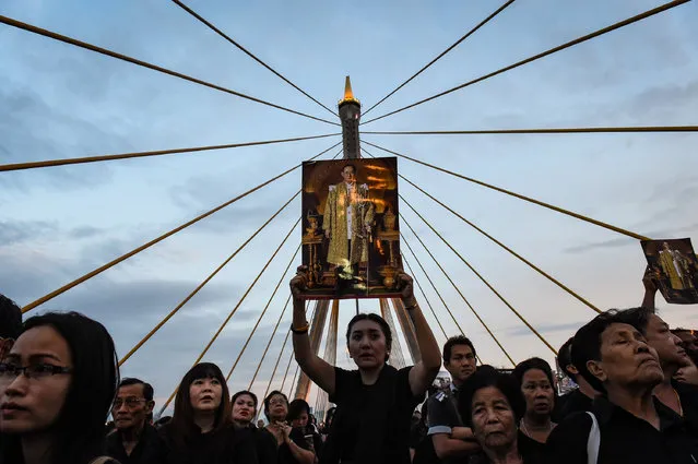 A woman holds aloft a picture of the late Thai King Bhumibol Adulyadej as people gather to commemorate his birthday on top of Bhumibol Bridge in Bangkok on December 5, 2016. (Photo by Lillian Suwanrumpha/AFP Photo)