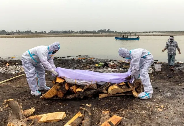 Men wearing protective suits place a white cloth over the body their relative, who died from the coronavirus disease (COVID-19), before his cremation on the banks of the river Ganges at Garhmukteshwar in the northern state of Uttar Pradesh, India, May 6, 2021. (Photo by Danish Siddiqui/Reuters)