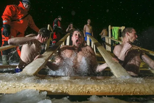 A rescue worker controls Russian Orthodox believers swimming in the icy water on Epiphany at a pond in Krasnoye Selo outside St.Petersburg, Russia, early Tuesday, January 19, 2016. The temperature in Krasnoye Selo is minus 16 Celsius (6.8 Fahrenheit). Thousands of Russian Orthodox Church followers plunged into icy rivers and ponds across the country to mark Epiphany, cleansing themselves with water deemed holy for the day. Water that is blessed by a cleric on Epiphany is considered holy and pure until next year's celebration, and is believed to have special powers of protection and healing. (Photo by Dmitry Lovetsky/AP Photo)