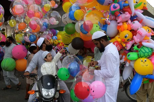 A child accompanying his parents buy baloons after offering special prayers on the occasion of Eid al-Fitr that marks the end of the holy month of Ramadan in Karachi on May 13, 2021. (Photo by Asif Hassan/AFP Photo)