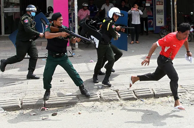 A Cambodian protester (R) runs as anti riot police officers fire tear gas during a clash between police and garment workers in Phnom Penh on November 12, 2013. One woman was shot dead and several injured in violent clashes between protesting garment workers and riot police in the Cambodian capital on November 12, a rights group and family members said. (Photo by AFP Photo)