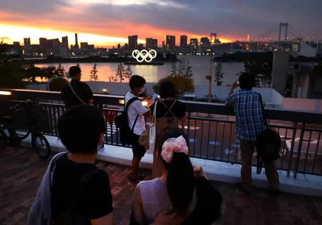 A person takes a photo of the Olympic Rings in front of the skyline during sunset, three days ahead of the official opening of the Tokyo 2020 Olympic Games, in Tokyo, Japan, July 20, 2021. (Photo by Kai Pfaffenbach/Reuters)