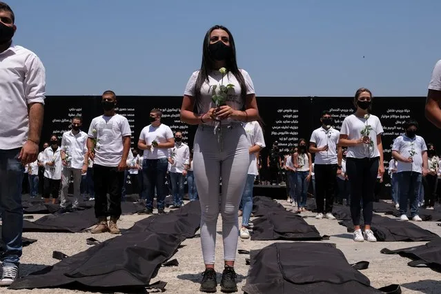 Students affiliated with the Lebanese Forces hold white roses and stand next to body bags in memory of the victims of last year's Beirut port blast, as Lebanon marks one-year anniversary of the explosion in Beirut, Lebanon on August 4, 2021. (Photo by Emilie Madi/Reuters)