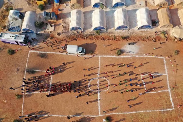 This aerial view shows young athletes gathered across a field at a camp for displaced Syrians during the so-called “Camp Olympics 2020” in the town of Fuaa, in the northwestern Syrian last major rebel bastion of Idlib, on August 7, 2021, as 120 boys from 12 different camps gather for their own version of the Olympic games, at the end of the Tokyo Olympics. (Photo by Omar Haj Kadour/AFP Photo)