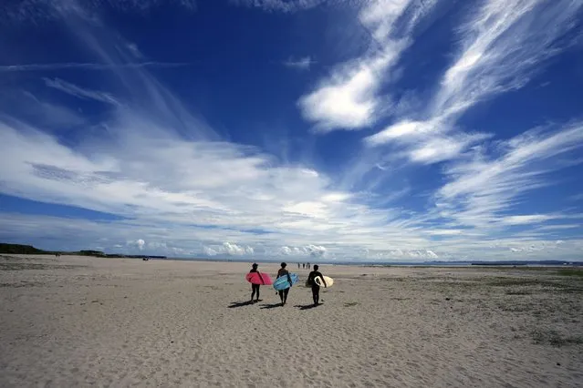 People walk on the beach to surf at the Yotsukura beach, about 30 kilometers (about 18 miles) south of the Fukushima Daiichi nuclear power plant, damaged by a massive March 11, 2011, earthquake and tsunami, in Iwaki, northeastern Japan, Saturday, Aug. 26, 2023. The Fukushima Daiichi nuclear power plant started releasing treated and diluted radioactive wastewater into the Pacific Ocean on last Thursday. (Photo by Eugene Hoshiko/AP Photo)