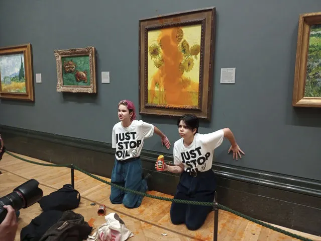 A handout picture from the Just Stop Oil climate campaign group shows activists with their hands glued to the wall under Vincent van Gogh's “Sunflowers” after throwing tomato soup on the painting at the National Gallery in central London on October 14, 2022. London's Metropolitan Police said its officers arrested two protesters from the Just Stop Oil group for criminal damage and aggravated trespass after they “threw a substance over a painting” at the gallery on Trafalgar Square. (Photo by Just Stop Oil/Handout via AFP Photo)