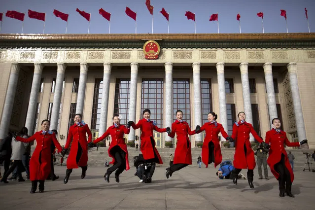 Hostesses, who facilitated the arrival of delegates by bus, leap as they pose for photographers in front of the Great Hall of the People during the opening session of China's annual National People's Congress (NPC) in Beijing, Saturday, March 5, 2016. (Photo by Mark Schiefelbein/AP Photo)