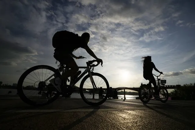 People wearing face masks to help curb the spread of the coronavirus are silhouetted as they ride bicycles near the Han River in Seoul, South Korea, Thursday, September 23, 2021. (Photo by Lee Jin-man/AP Photo)