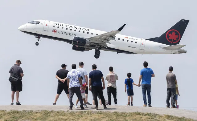 People watch an Air Canada plane take off at Trudeau Airport from Jacques de Lesseps Park in Montreal, Sunday, June 11, 2023. Signs warning people that the consumption of food is prohibited have been erected at the plane spotting park to deter the gathering of birds. (Photo by Graham Hughes/The Canadian Press via AP Photo)