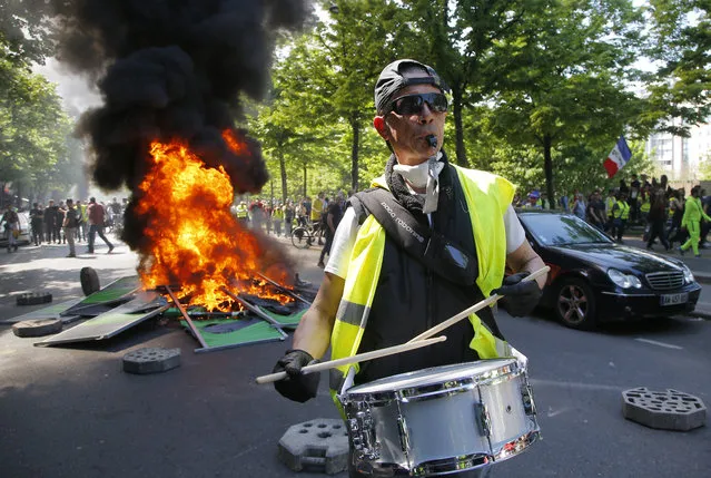 A man bangs a drum in front of a fire on the street during a yellow vest demonstration in Paris, Saturday, April 20, 2019. French yellow vest protesters are marching anew to remind the government that rebuilding the fire-ravaged Notre Dame Cathedral isn't the only problem the nation needs to solve. (Photo by Michel Euler/AP Photo)