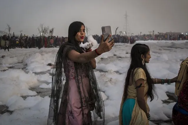 A Hindu devotee takes a selfie while holding handful of chemical foam she picked from Yamuna river during Chhath Puja festival in New Delhi, India, Wednesday, November 10, 2021. A vast stretch of one of India's most sacred rivers, the Yamuna, is covered with toxic foam, caused partly by high pollutants discharged from industries ringing the capital New Delhi. Still, hundreds of Hindu devotees Wednesday stood knee-deep in its frothy, toxic waters, sometimes even immersing themselves in the river for a holy dip, to mark the festival of Chhath Puja. (Photo by Altaf Qadri/AP Photo)