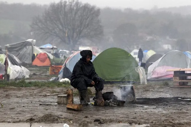 A refugee warms herself next to a bonfire under heavy rainfall in a makeshift camp for refugees and migrants at the Greek-Macedonian border near the village of Idomeni, Greece, March 23, 2016. (Photo by Alexandros Avramidis/Reuters)