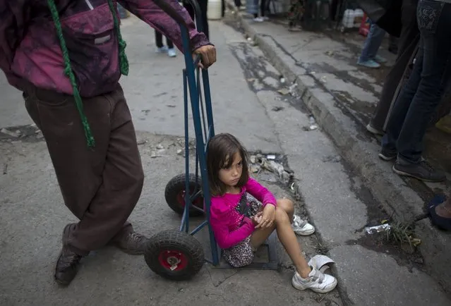 A girl sits on a two-wheeled dolly as she waits with others to fill their containers with water, in Caracas, Venezuela, Monday, April 1, 2019. (Photo by Ariana Cubillos/AP Photo)