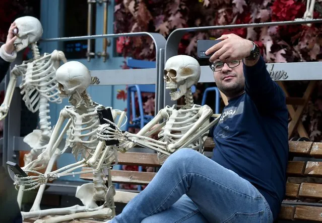 A man takes a selfie outside a restaurant decorated with skeletons for the upcoming Halloween party, in Kiev, on October 29, 2021. (Photo by Sergei Supinsky/AFP Photo)