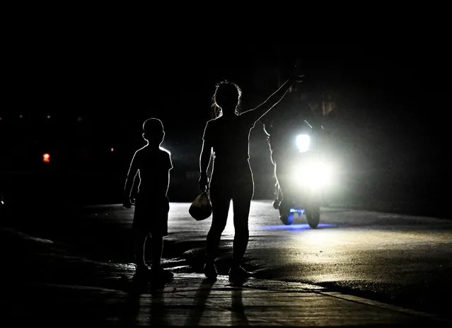 A woman with her son signals a car on a dark street during a blackout in Bauta municipality, Artemisa province, Cuba, on March 18, 2024. (Photo by Yamil Lage/AFP Photo)