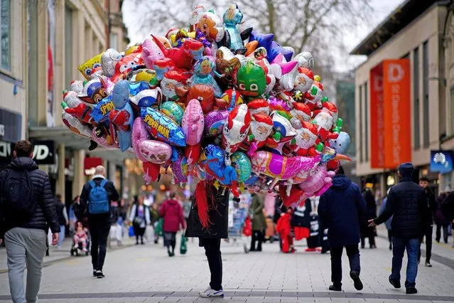 A balloon vendor is passed by Christmas shoppers in the centre of Cardiff, Wales on Thursday, December 16, 2021, where people have been told to prepare for more restrictions in the coming weeks as the country faces an impending “tsunami” from the Omicron variant of Covid-19. (Photo by Ben Birchall/PA Images via Getty Images)