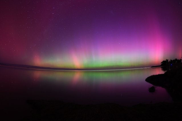 The Aurora Australis, also known as the Southern Lights, glow on the horizon over waters of Lake Ellesmere on the outskirts of Christchurch on May 11, 2024. (Photo by Sanka Vidanagama/AFP Photo)