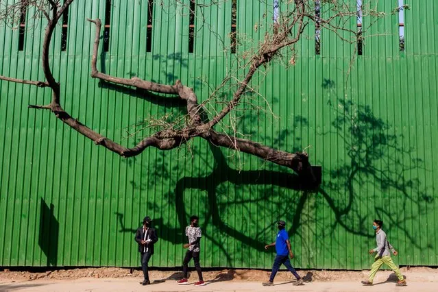 Men walk along a street past a construction site fence in New Delhi on March 9, 2022. (Photo by Xavier Galiana/AFP Photo)