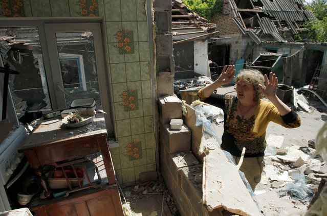 A woman inspects debris while standing outside her damaged house, which according to locals was caused by recent shelling, in the village of Staromikhailovka, outside the separatist-held city of Donetsk, Ukraine, May 24, 2016. (Photo by Alexander Ermochenko/Reuters)