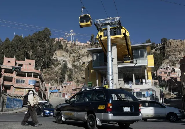 Traffic and a pedestrian move under the cable car station at Kota Uma in La Paz, July 23, 2015. Bolivia already has the largest urban cable car system in the world. Now the booming country is tripling the size of the network and will soon have nine lines whizzing above the administrative capital of La Paz. (Photo by David Mercado/Reuters)