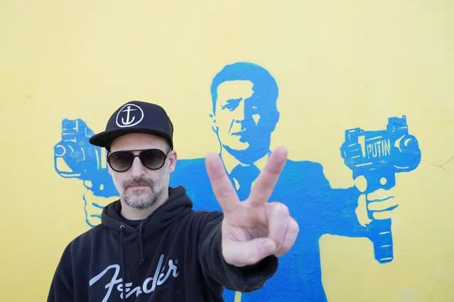 Street artist Todd Goodman, known as 1GoodHombre, stands in front of his stencil of Ukrainian President Volodymyr Zelenskyy holding submachine guns, painted without a permit on a building's wall in Santa Monica, Calif., on Monday, March 21, 2022. Goodman came out of anonymity as a street artist, risking arrest and fines for his unlicensed work to solicit funds for Ukrainian war refugees. (Photo by Eugene Garcia/AP Photo)