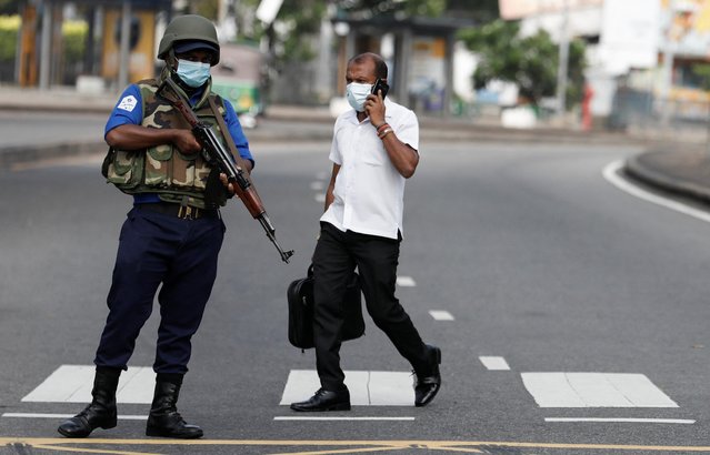 A navy soldier stands guard at a check point as a man walks past him to work place on the main road after the curfew was extended for another extra day following a clash between Anti-government demonstrators and Sri Lanka's ruling party supporters, amid the country's economic crisis, in Colombo, Sri Lanka, May 11, 2022. (Photo by Dinuka Liyanawatte/Reuters)