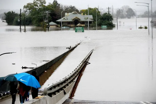 People look out towards flooded houses next to an old Windsor Bridge along the overflowing Hawkesbury River in the northwestern Sydney suburb of Windsor on July 6, 2022. Thousands of Australians were ordered to evacuate their homes in Sydney as torrential rain battered the country's largest city and floodwaters inundated its outskirts. (Photo by Muhammad Farooq/AFP Photo)
