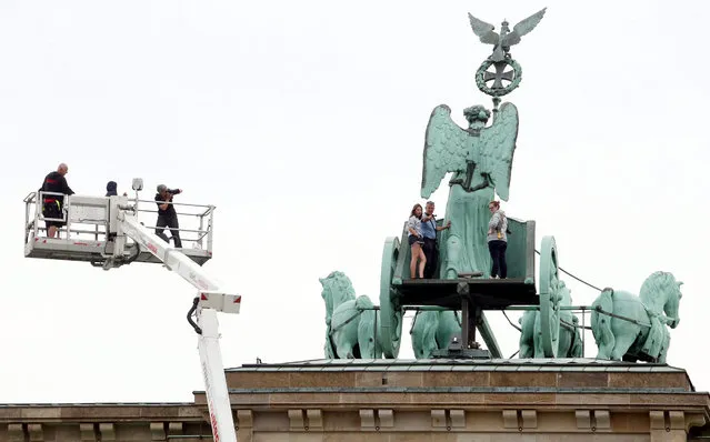 People take souvenir pictures after carrying out maintenance work on the statue of a quadriga, a chariot drawn by four horses, located on top of the Brandenburg Gate, one of the major landmarks of Berlin, Germany, 18 August 2015. (Photo by Wolfgang Kumm/EPA)
