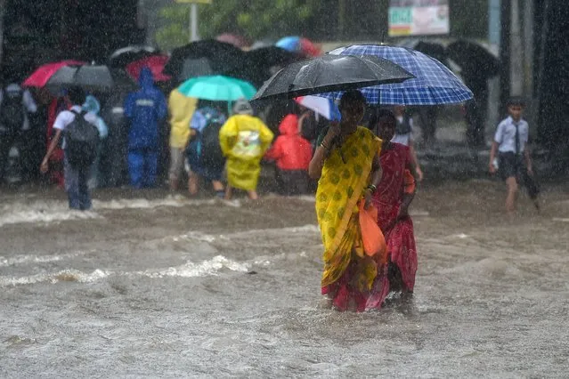 Pedestrians walk through flooded street during rain showers in Mumbai on July 5, 2022. (Photo by Punit Paranjpe/AFP Photo)