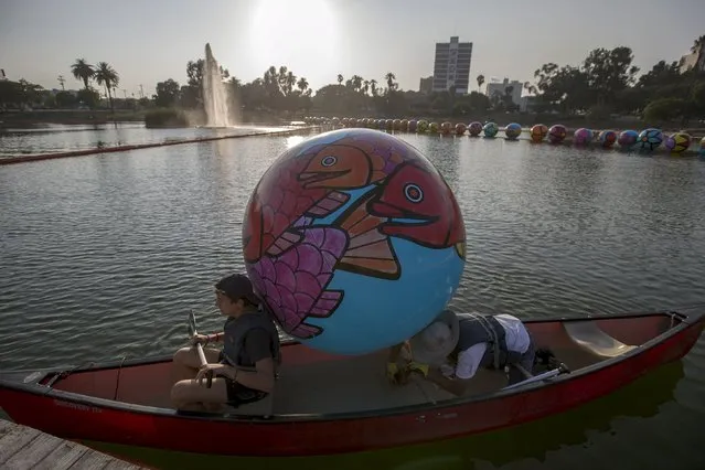 Volunteers transport an inflated sphere into a canoe to be lowered in MacArthur Park Lake during the installation of Portraits of Hope's exhibition “Spheres at MacArthur Park” in Los Angeles, California August 21, 2015. (Photo by Mario Anzuoni/Reuters)